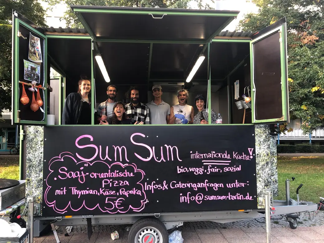 Sieben Menschen aus dem SumSum-Team lachen im geöffneten Anhänger