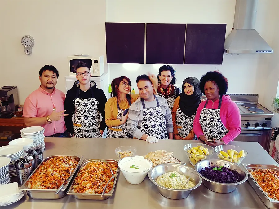 Sieben Menschen aus dem SumSum-Team in Schürzen hinter einem Buffet mit Reis, Joghurt und Rotkohl